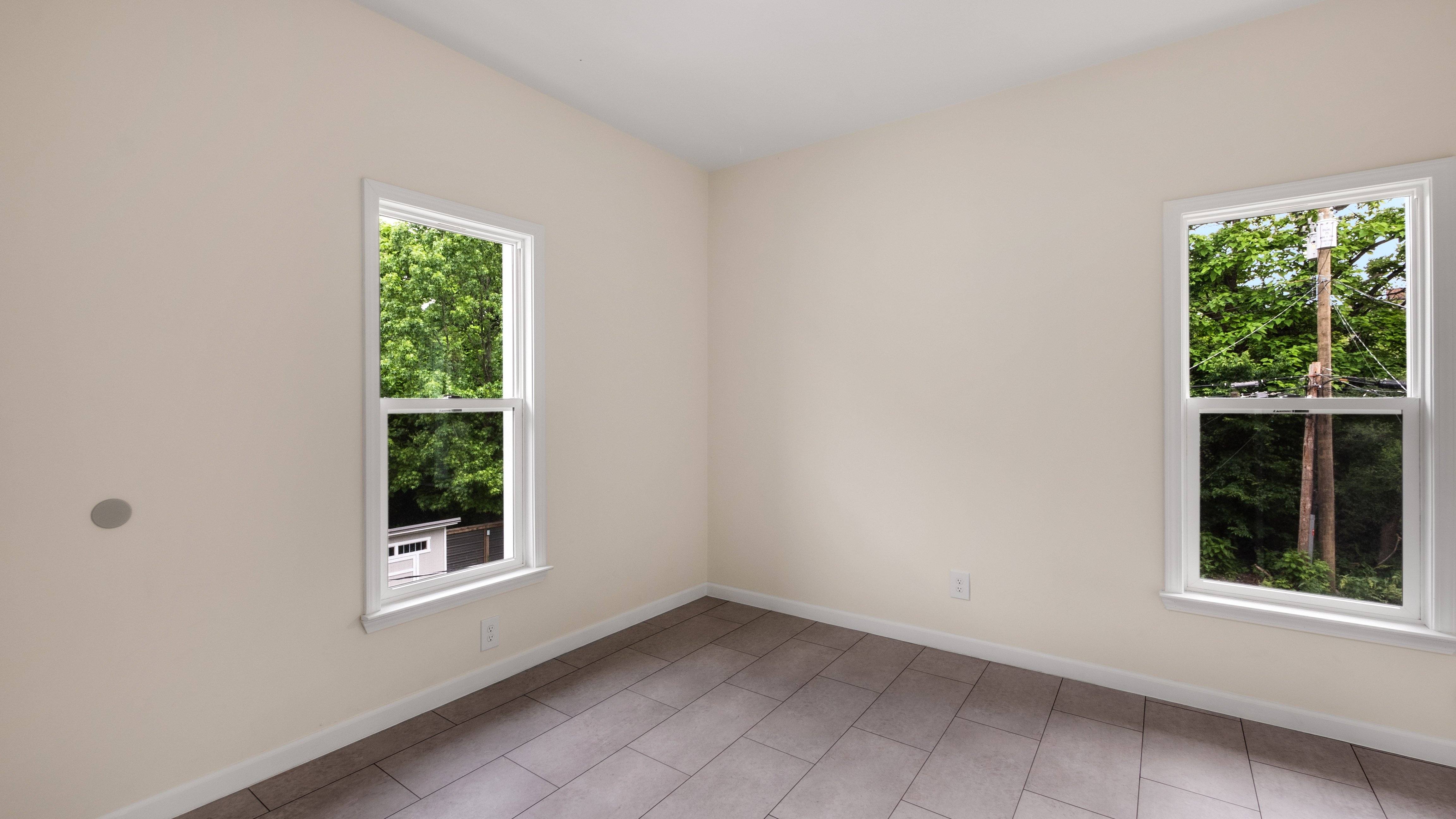 A room with two windows showing a view of trees and a building.